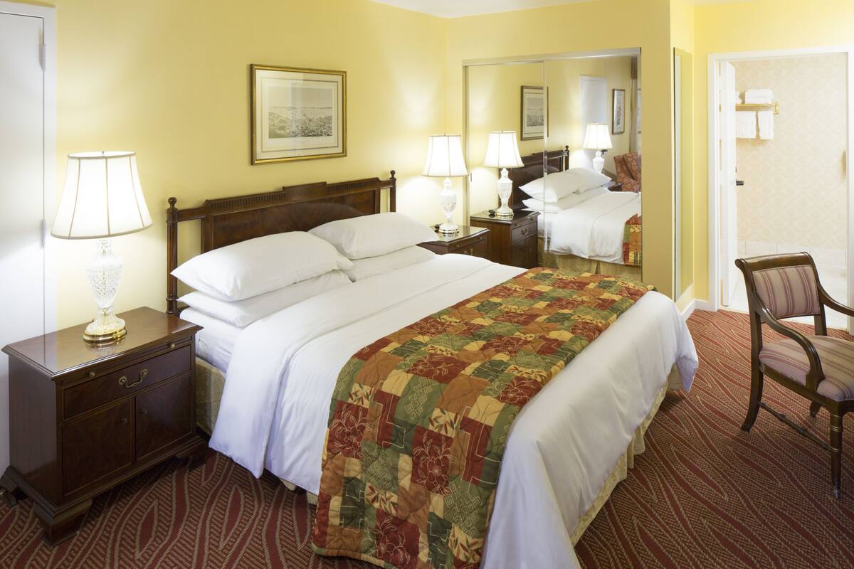 A hotel room with a large bed, two bedside tables with lamps, a chair, and a mirror.