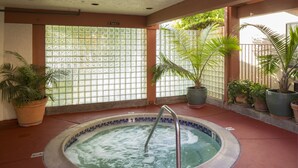 Un bain à remous avec un escalier en métal, entouré de plantes en pot et bordé d’un mur carrelé à motifs géométriques.