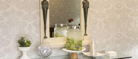 A glass-top console table with decorative items, a mirror above it, and patterned wallpaper.
