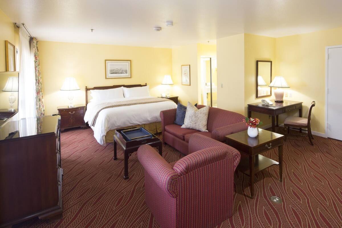 A hotel room with a bed, two armchairs, a small table, a desk, and a lamp.