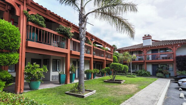 Un hôtel à plusieurs étages doté de balcons, de plantes en pot et d’un espace de stationnement.