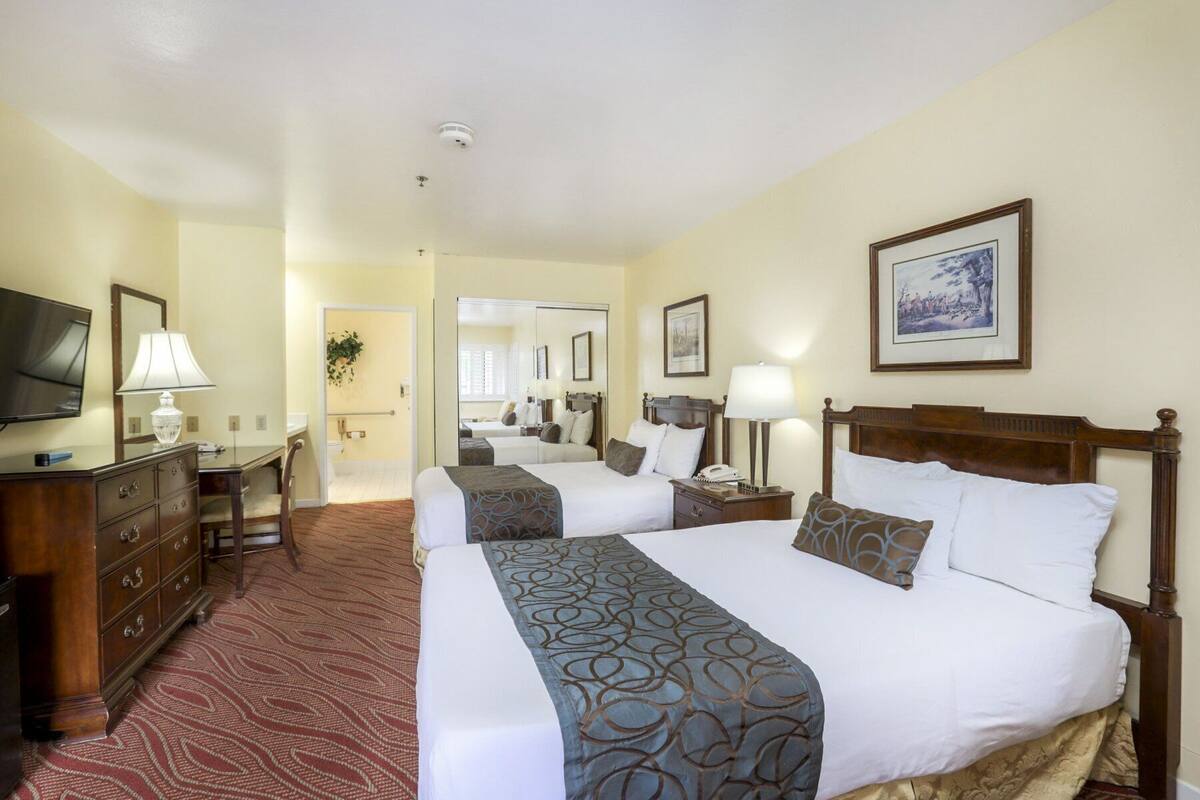 A hotel room with two beds, a desk, a TV, and a mirror.