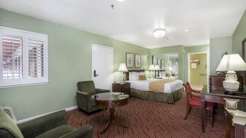 A hotel room with a bed, two chairs, a desk, a mirror, and a window with blinds.