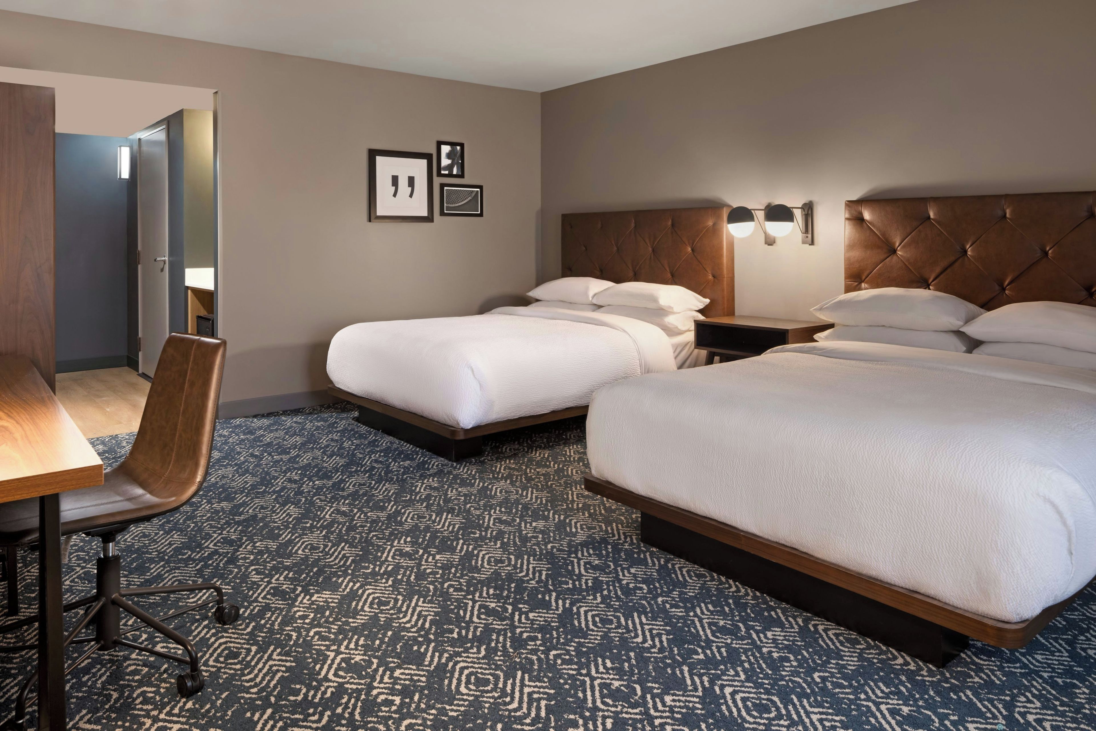 Habitación de hotel con dos camas, un escritorio, una silla y una alfombra estampada.