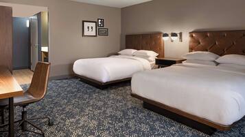 Habitación de hotel con dos camas, un escritorio, una silla y una alfombra estampada.