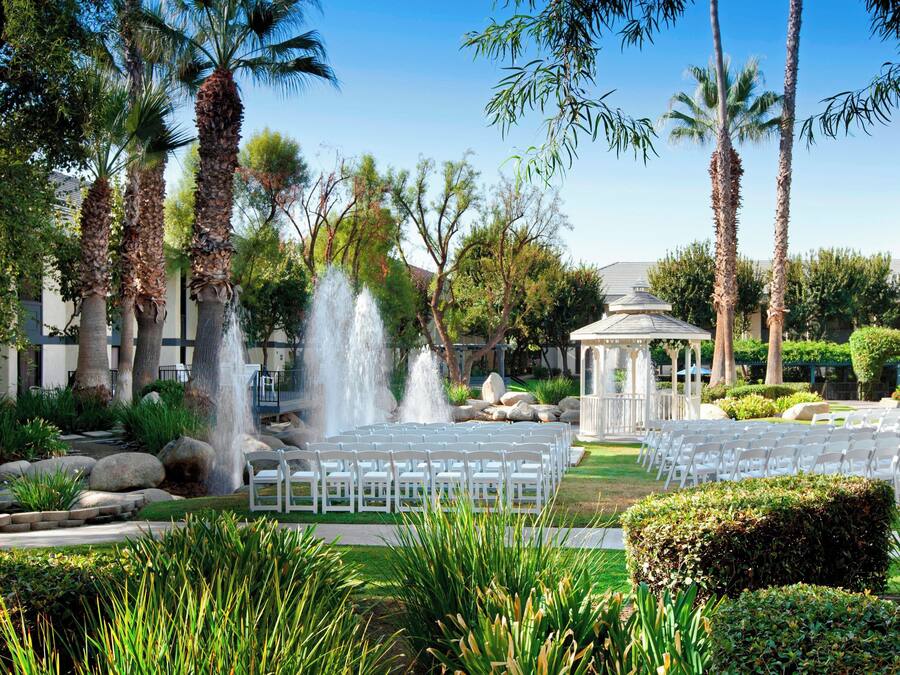 An outdoor wedding venue with a fountain, palm trees, and a gazebo.