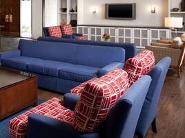 Un salon moderne avec un canapé bleu, des coussins aux motifs rouges et blancs, une table basse en bois et un téléviseur à écran plat fixé au mur.