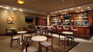 A bar area with multiple seating options, a television mounted on the wall, and a variety of bottles on shelves. - Four Points by Sheraton Bakersfield (Bakersfield)