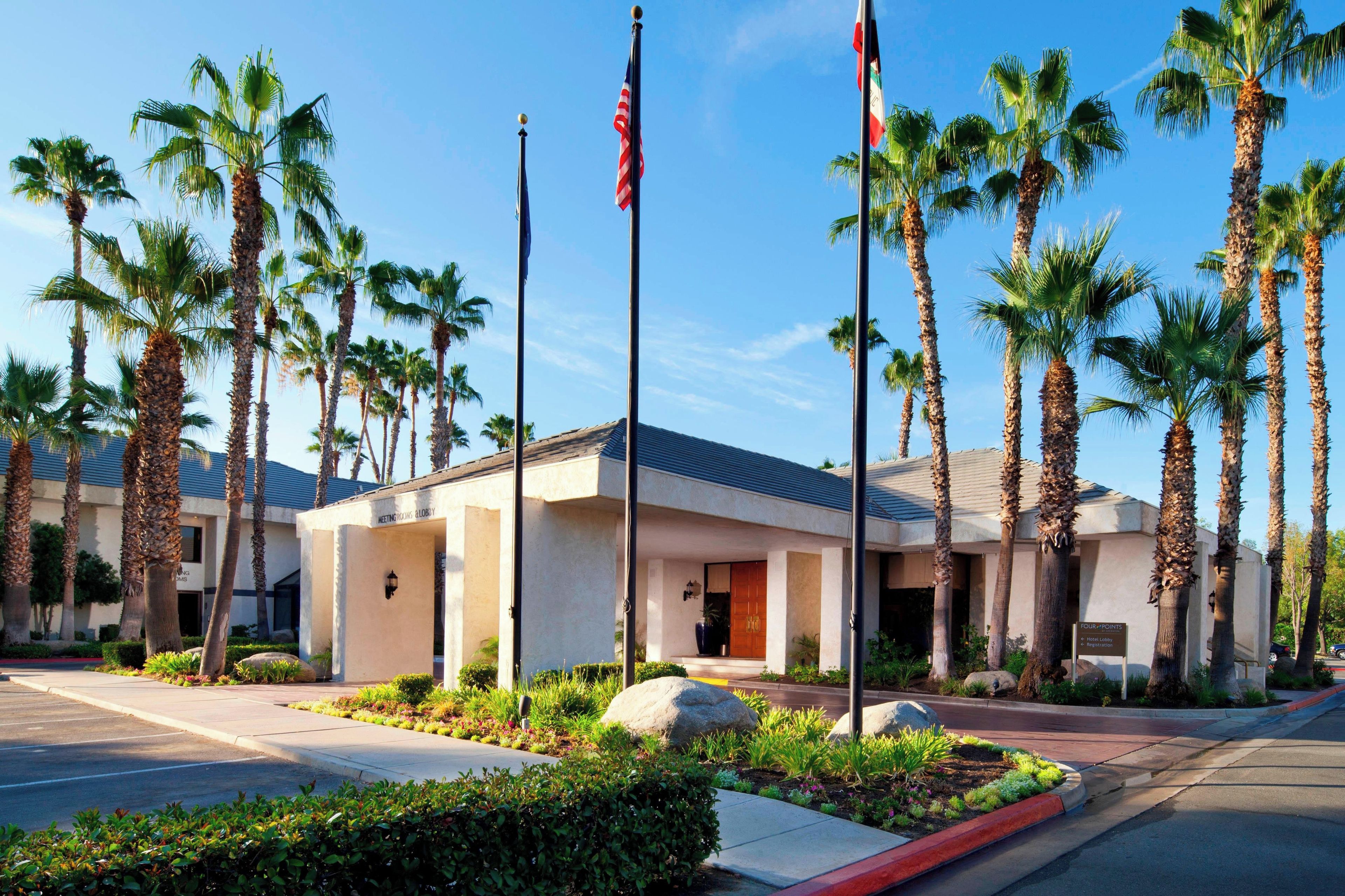 A hotel with a modern design, featuring palm trees and a clear blue sky.
