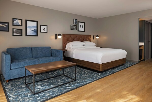 A hotel room with a bed, a blue sofa, a wooden coffee table, and a patterned rug.