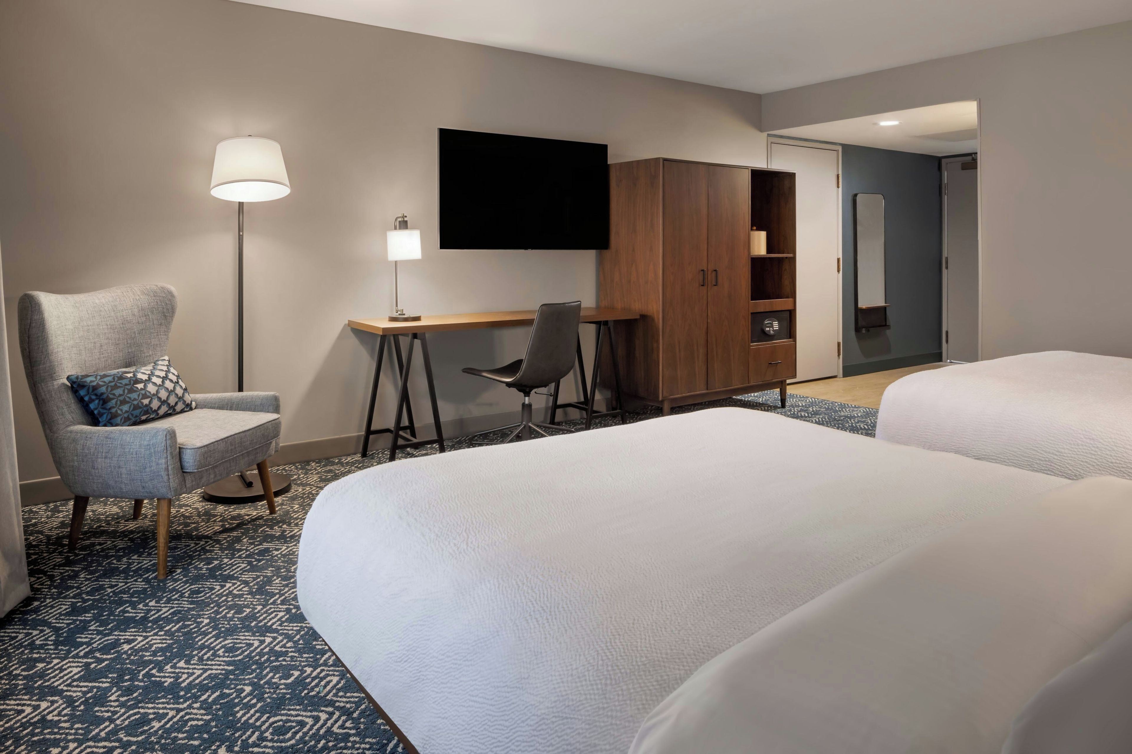 Een hotelkamer met twee bedden, een bureau, een stoel, een televisie en een kledingkast.