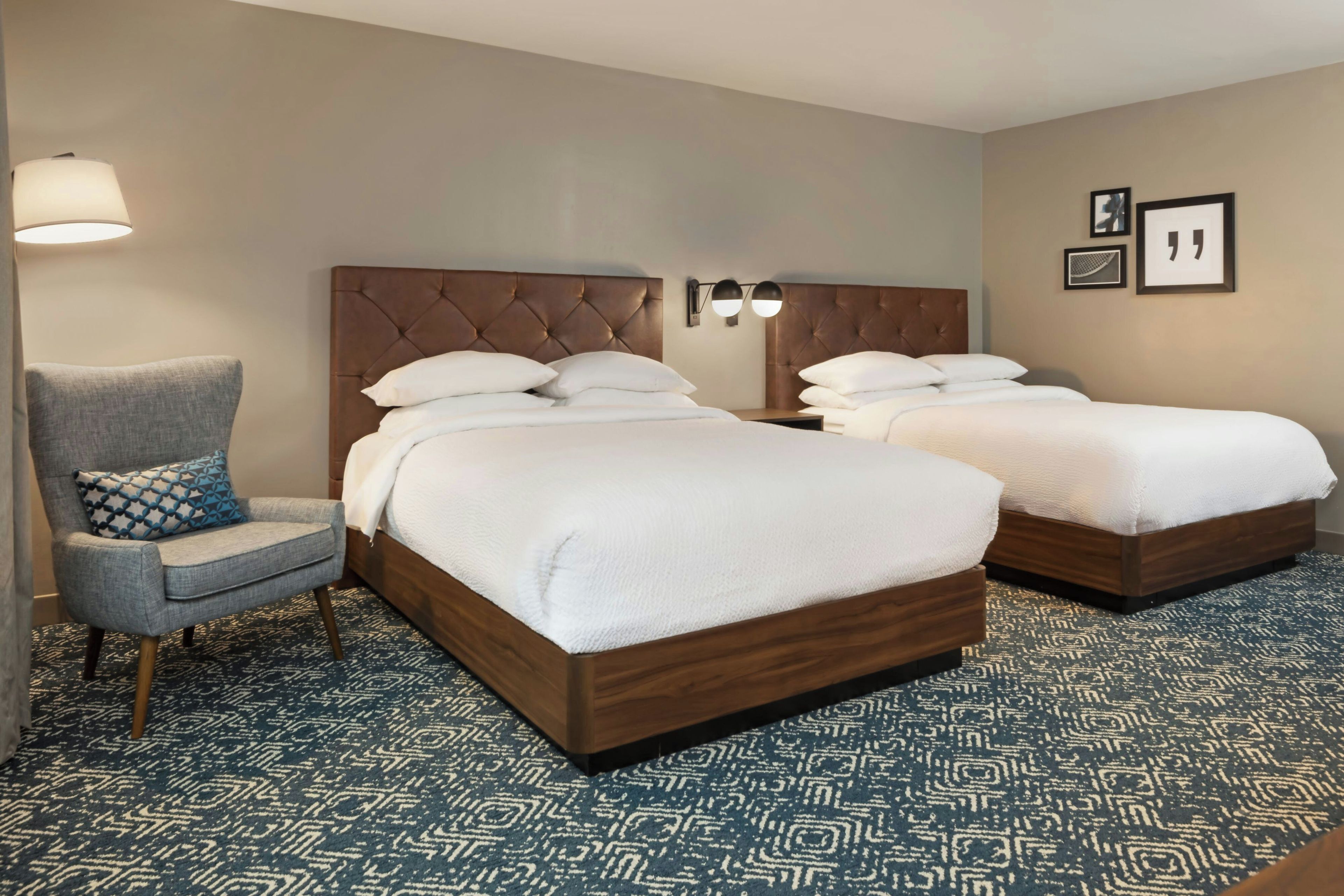 A hotel room with two beds, a chair, and a patterned carpet.