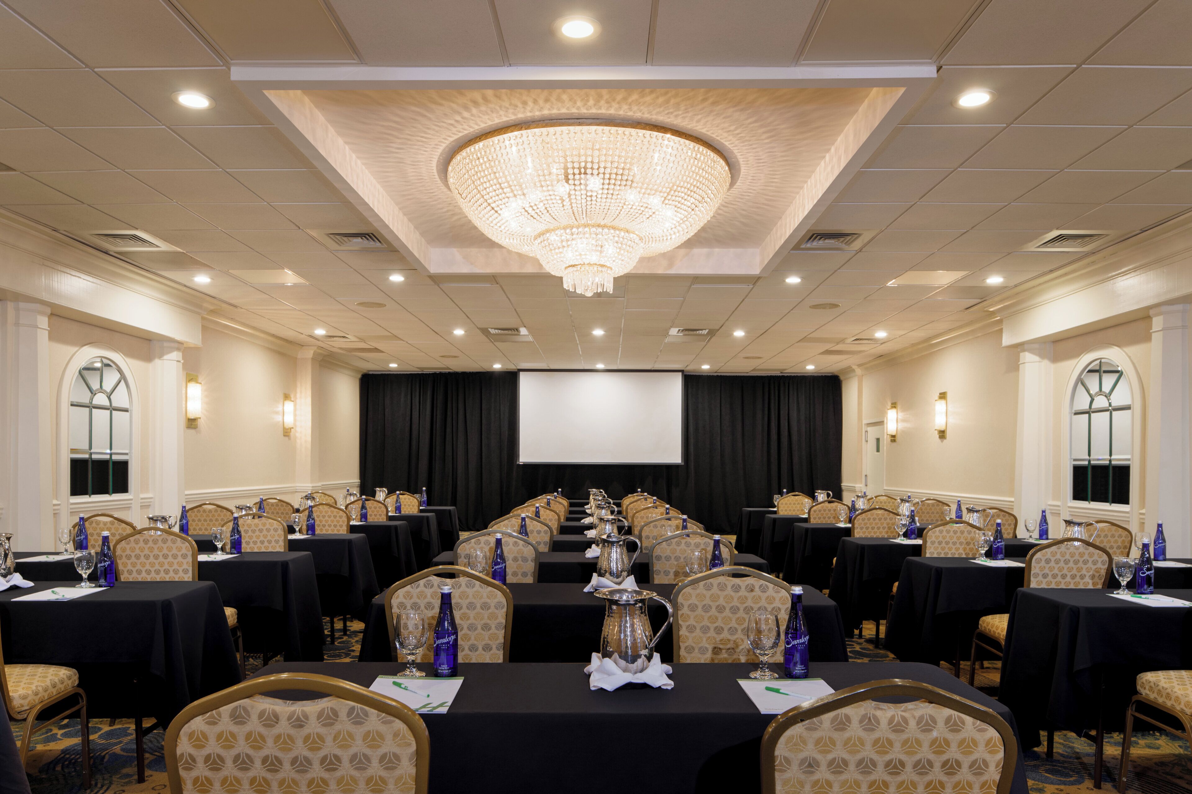 A conference room with a large chandelier, multiple tables with chairs, and a screen at the front.