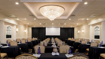 A conference room with a large chandelier, multiple tables with chairs, and a screen at the front.