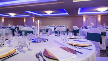 Een feestzaal met ronde tafels gedekt voor een diner, elk voorzien van bestek, borden en glazen.