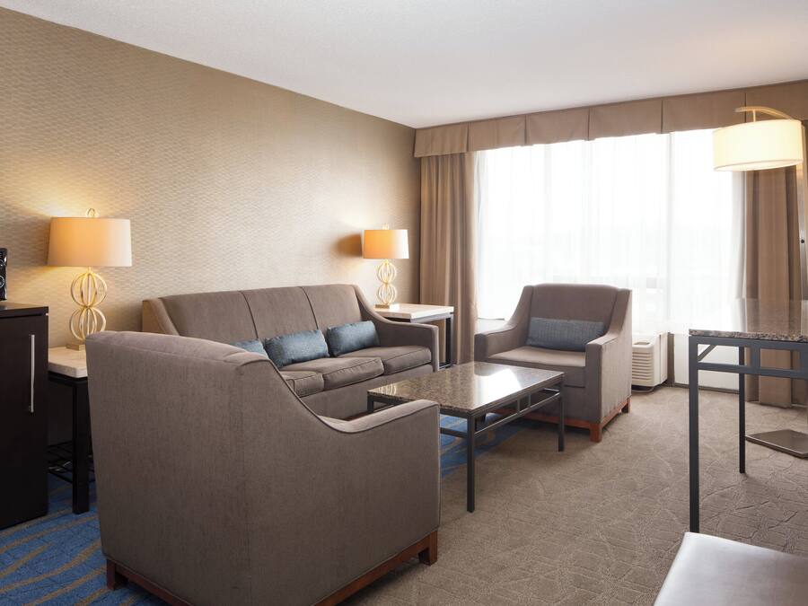 A hotel room with a sofa, armchair, coffee table, TV, and lamps.