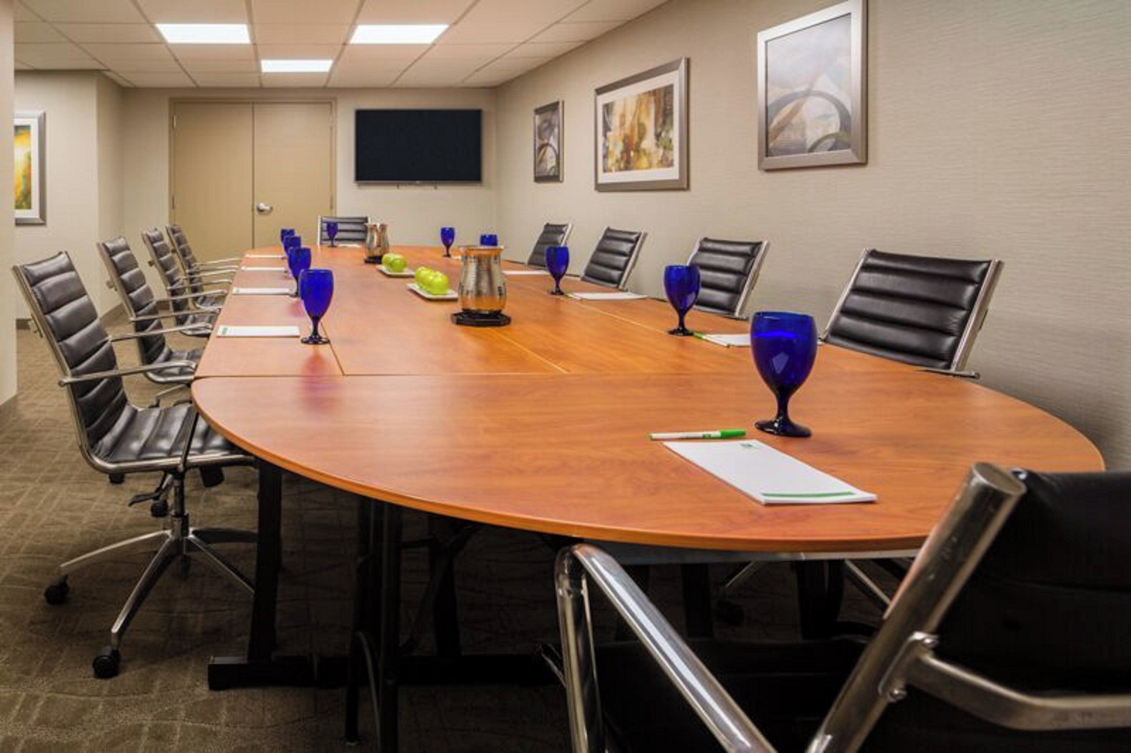 A conference room with a long table, chairs, and a flat-screen TV on the wall.