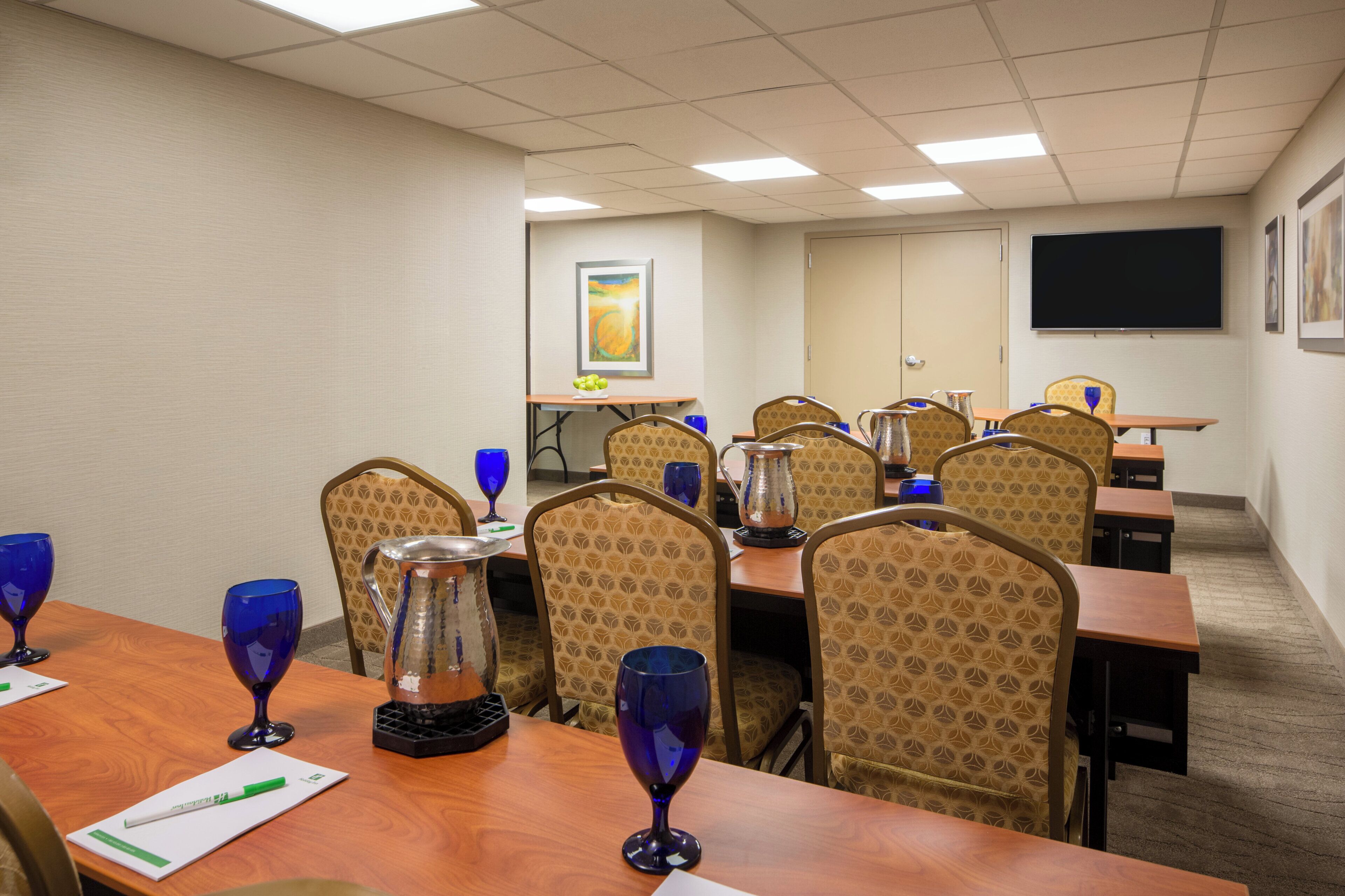 A conference room with a long table, chairs, a projector screen, and a painting on the wall.