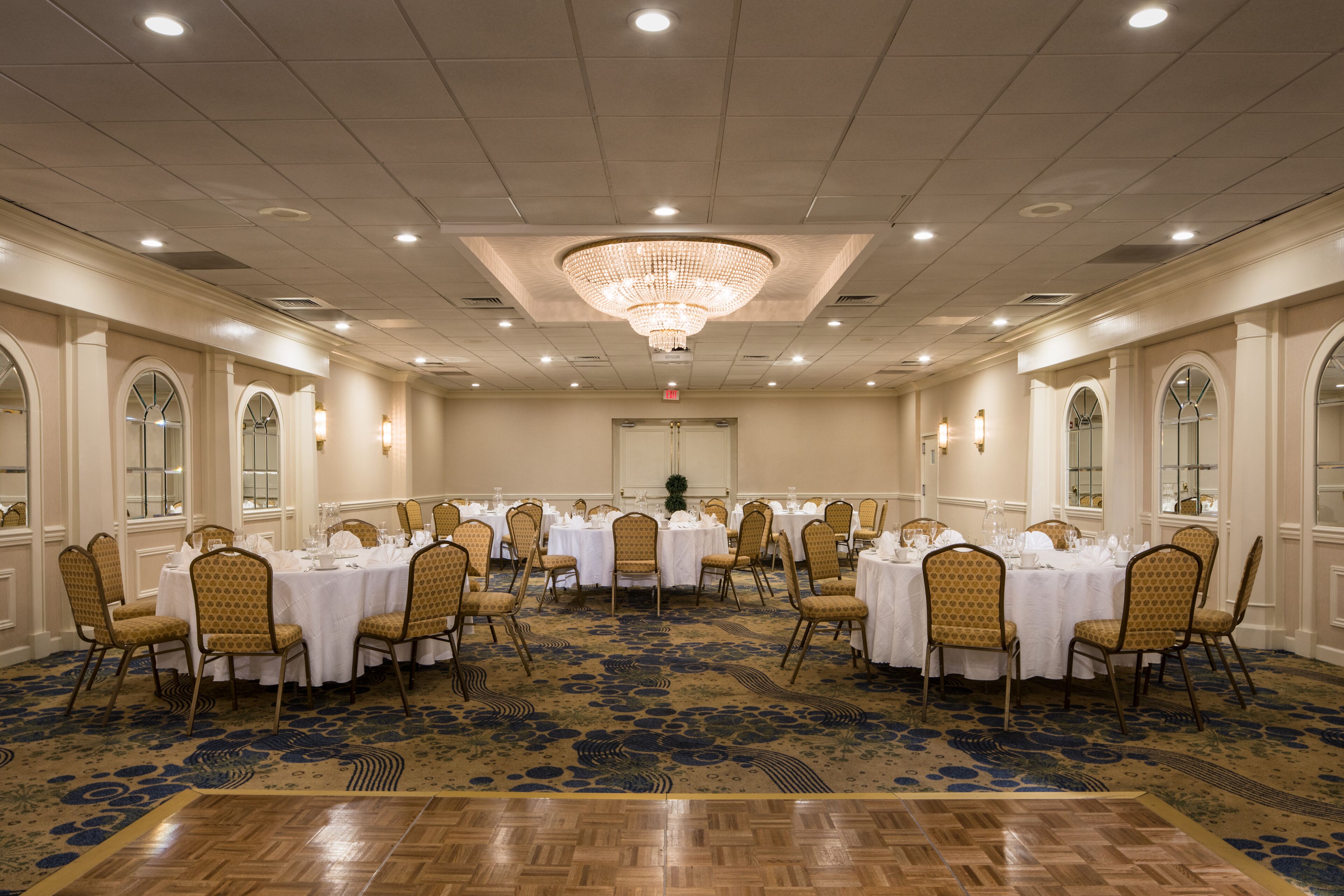 A banquet hall with round tables, chairs, and a chandelier.