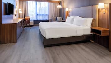 A modern hotel room with a large bed, a desk, a chair, and a TV.