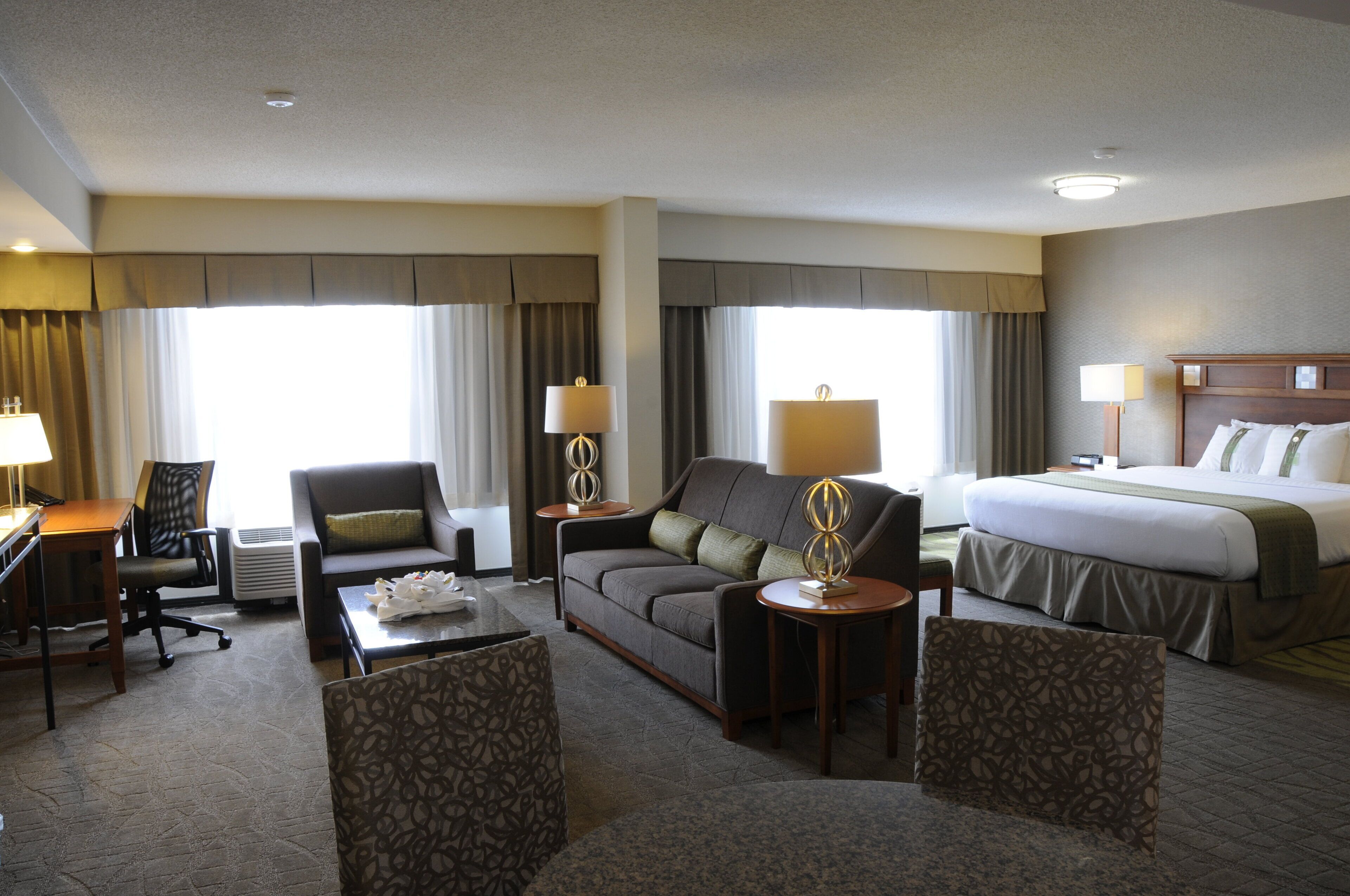 A hotel room with a bed, two armchairs, a sofa, a desk, and two lamps.