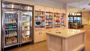 Cocina de hotel con refrigerador, microondas y despensa llena de bocadillos y bebidas.