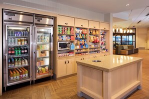 Cocina de hotel con refrigerador, microondas y despensa llena de bocadillos y bebidas.