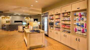 Quarto de hotel com cozinha compacta, área de estar e minibar repleto de lanches e bebidas.