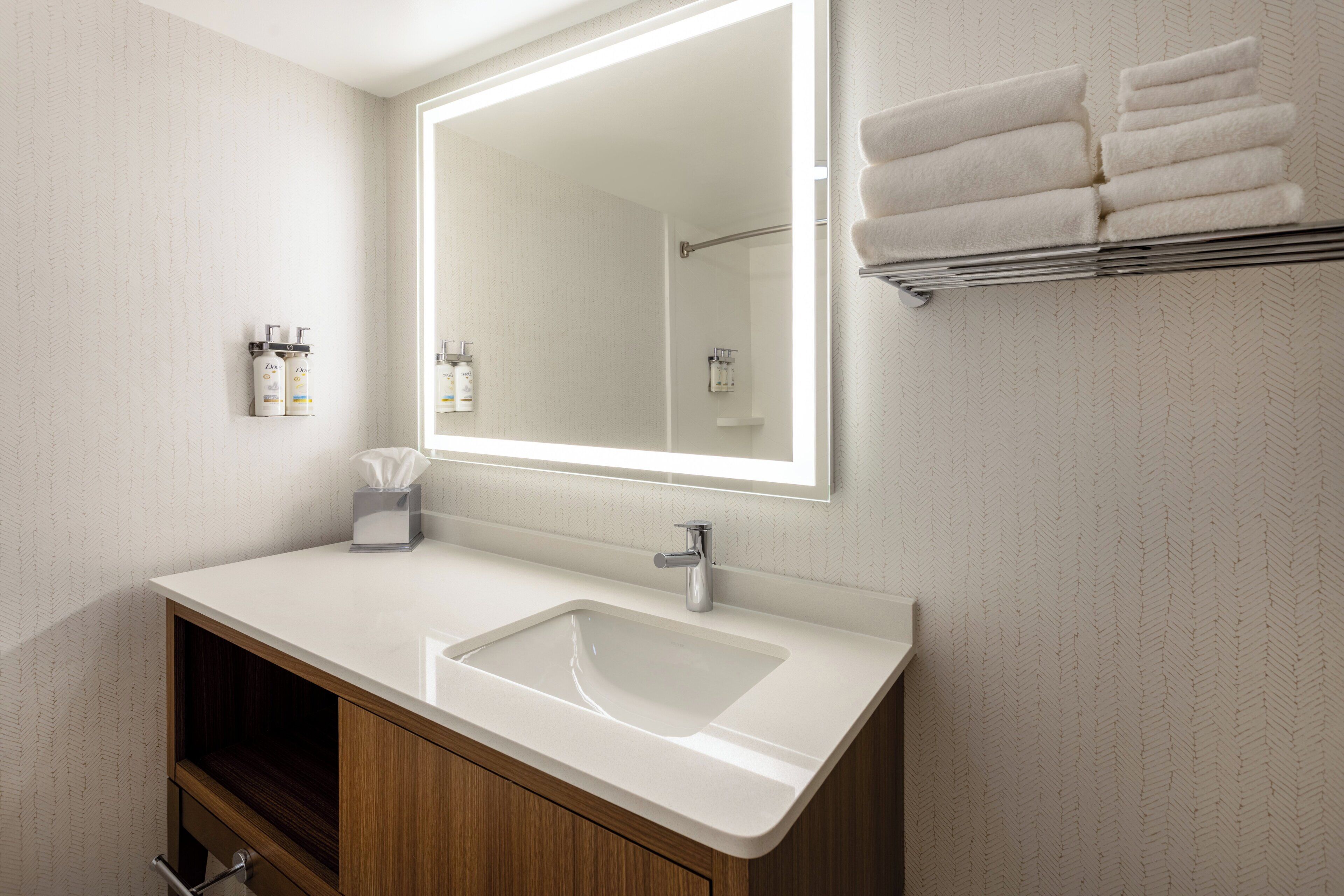 A modern bathroom with a large mirror, white sink, and wooden cabinets.