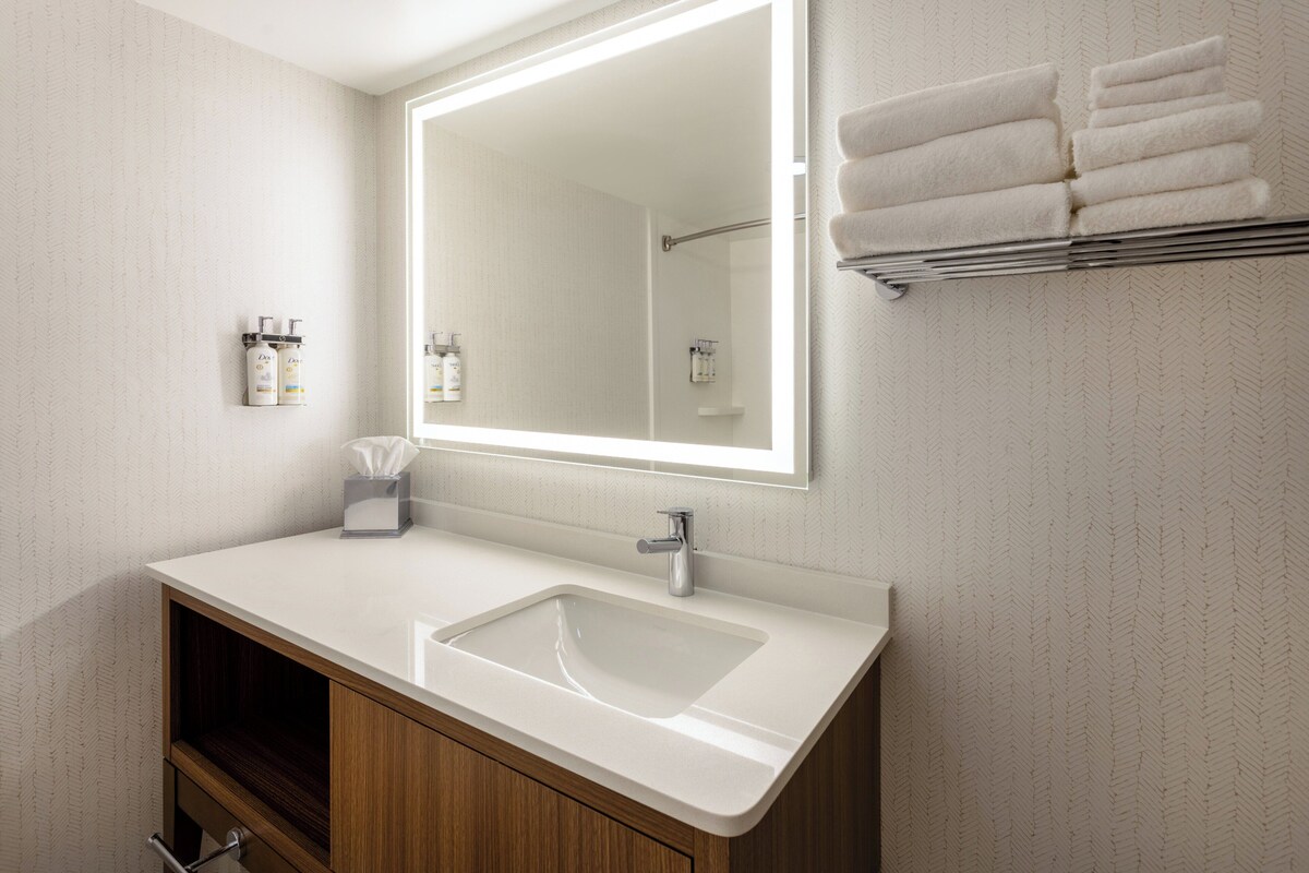 A modern bathroom with a large mirror, white sink, and wooden cabinets.