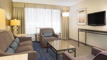 A hotel room with a sofa, armchair, a small table, a TV, and a lamp.