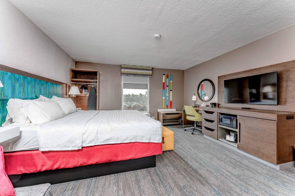 A hotel room with a bed, desk, TV, and storage unit.