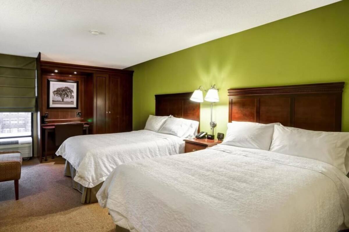 A hotel room with two beds, a desk, a chair, and a window with a view.