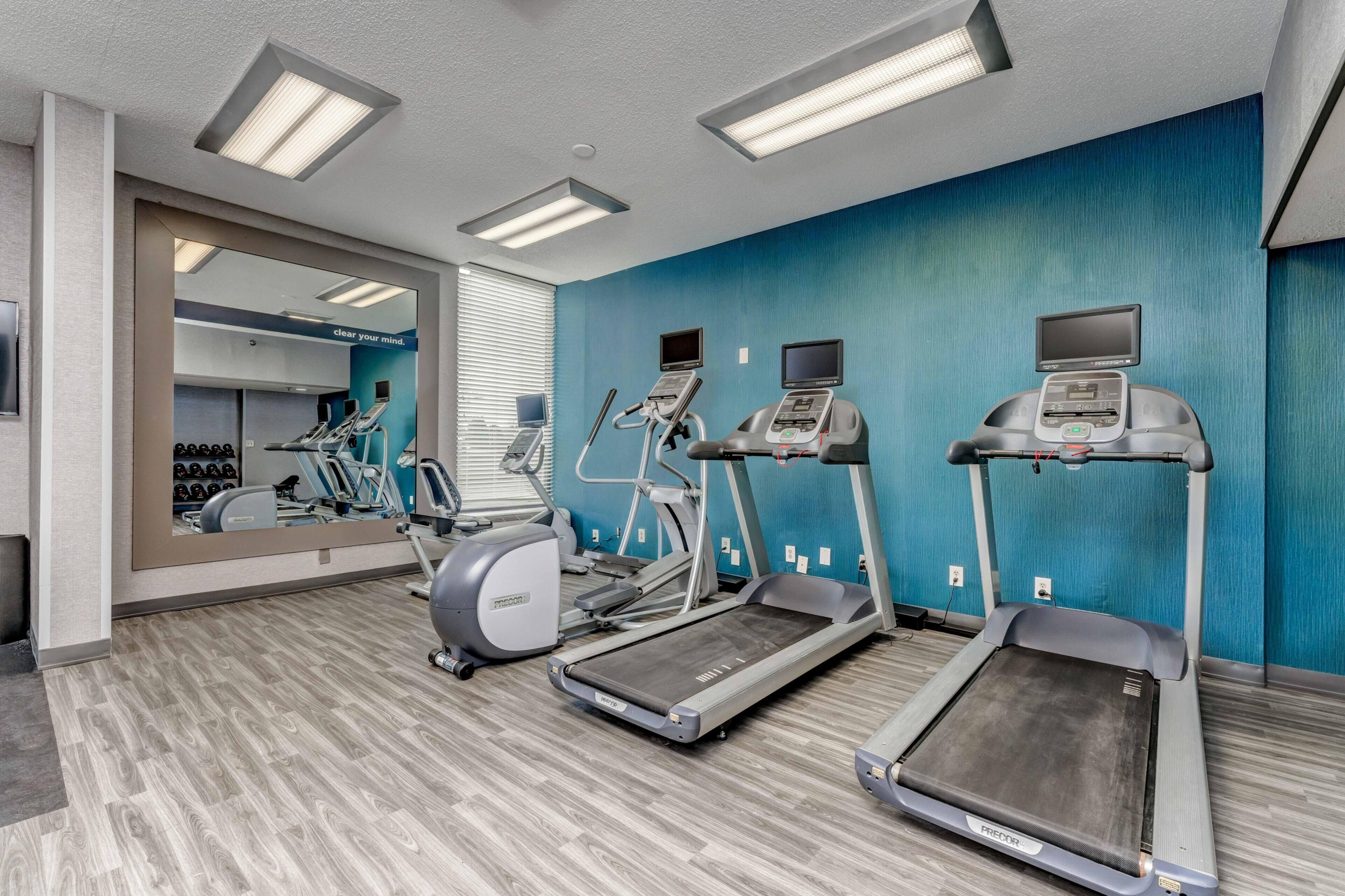 A gym with treadmills, elliptical machines, and a mirrored wall.