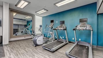 A gym with treadmills, elliptical machines, and a mirrored wall.