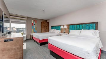 Habitación de hotel con dos camas, un escritorio, un ventanal y vistas a la ciudad.