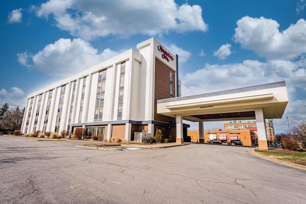 A Hampton Inn hotel with a gas station, large parking lot, and a clear sky.