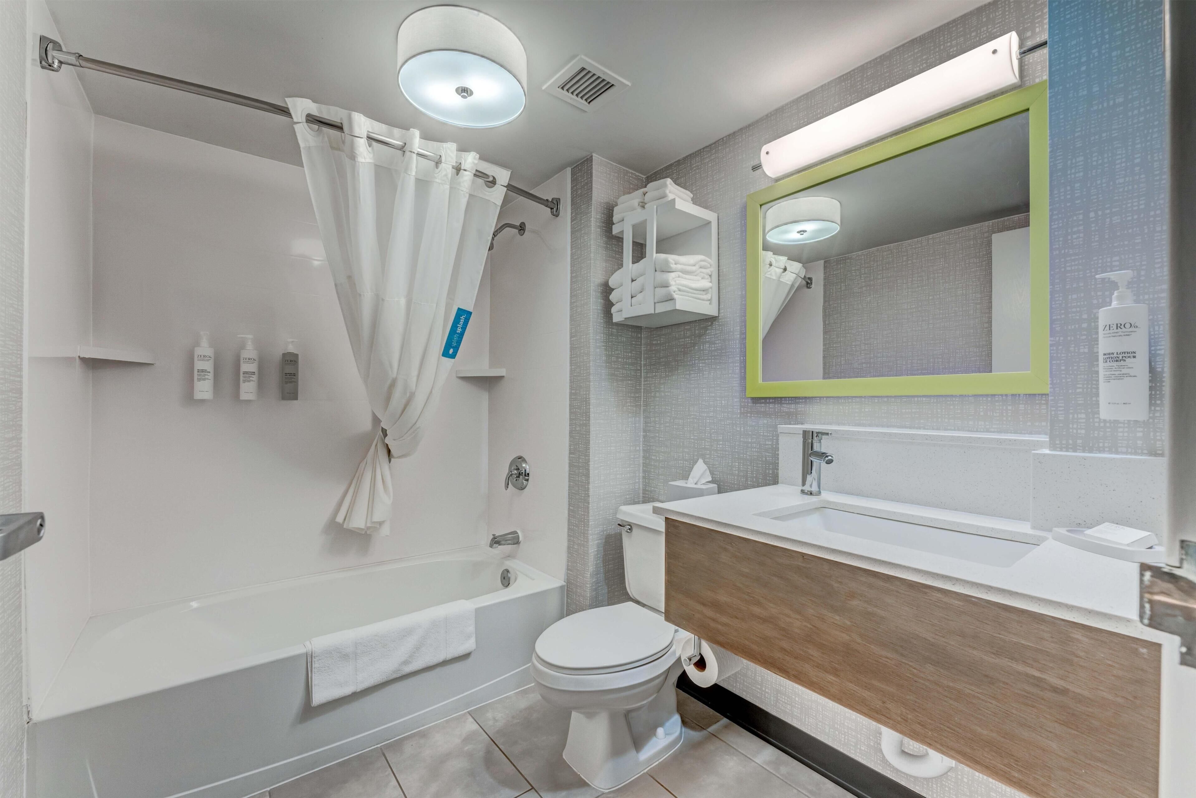 Une salle de bain moderne équipée d’une baignoire, de toilettes et d’un lavabo, avec un miroir, un porte-serviettes et des articles de toilette.