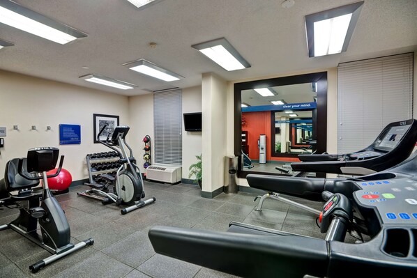A gym with exercise equipment, a television, and a mirror.