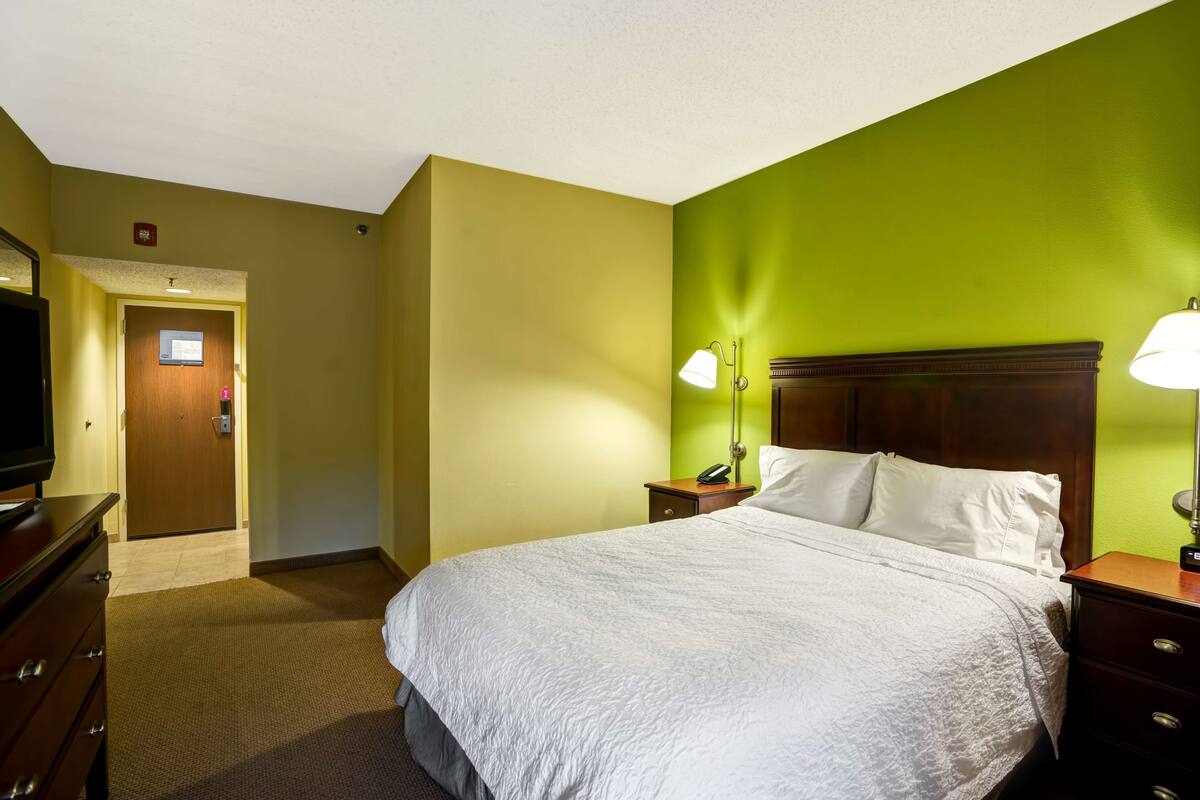 A hotel room with a bed, bedside tables, a TV, and a door leading to the hallway.