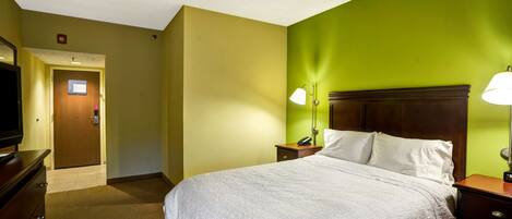 Une chambre d’hôtel comprenant un lit, des tables de chevet, une télévision et une porte donnant sur le couloir.