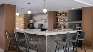 Zona de bar moderna con un muro de acento de piedra, taburetes, un televisor de pantalla plana y una variedad de botellas de licor.