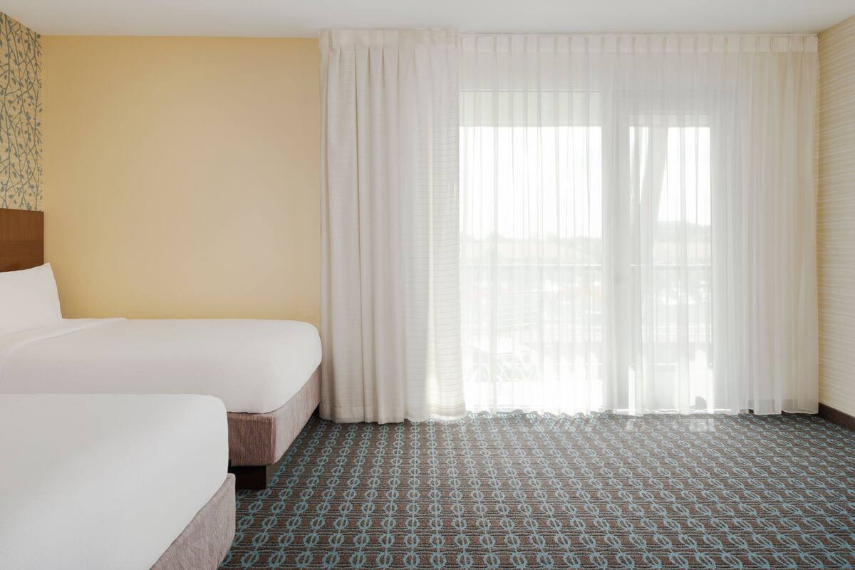 A hotel room with a bed, a window with sheer curtains, and a patterned carpet.