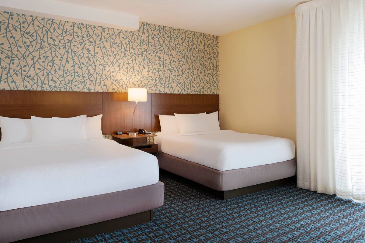 A hotel room with two beds, a nightstand, a lamp, and a patterned carpet.