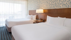 Habitación de hotel con dos camas, cabecero de madera, mesita de noche con lámpara y pared con estampado.