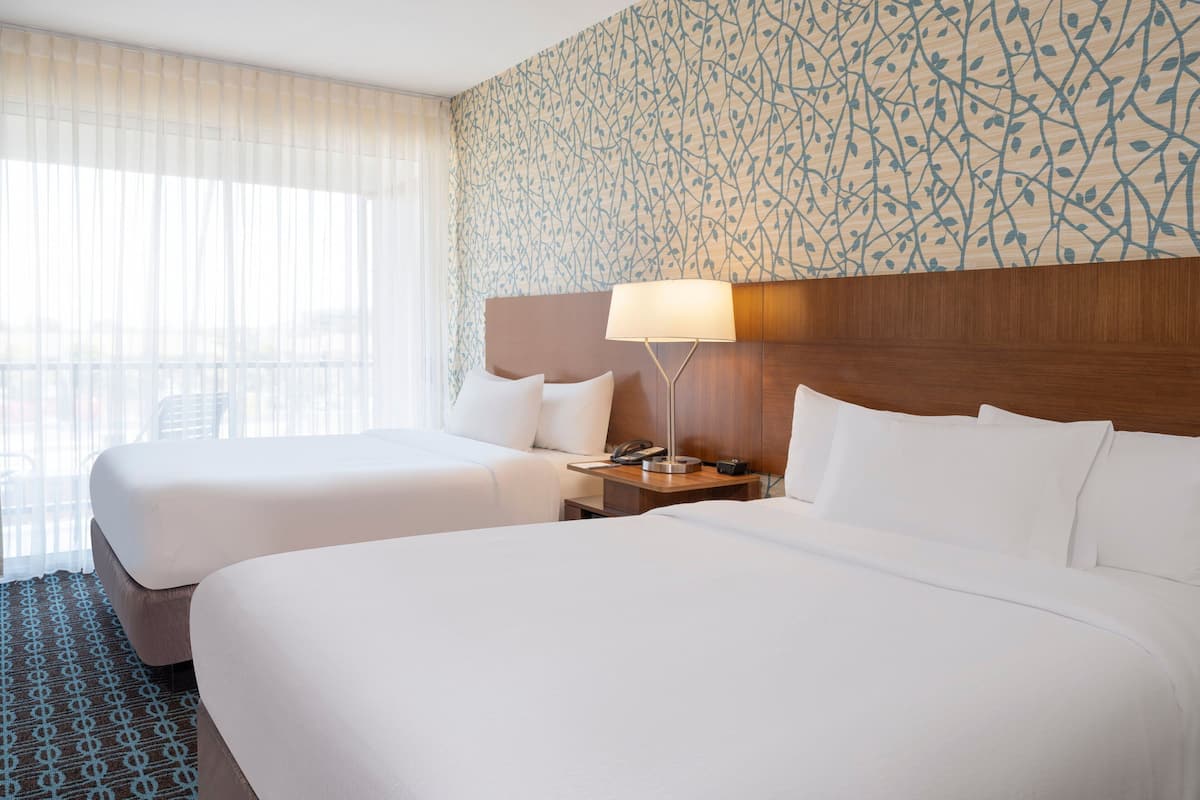 A hotel room with two beds, a wooden headboard, a bedside table with a lamp, and a patterned wall.