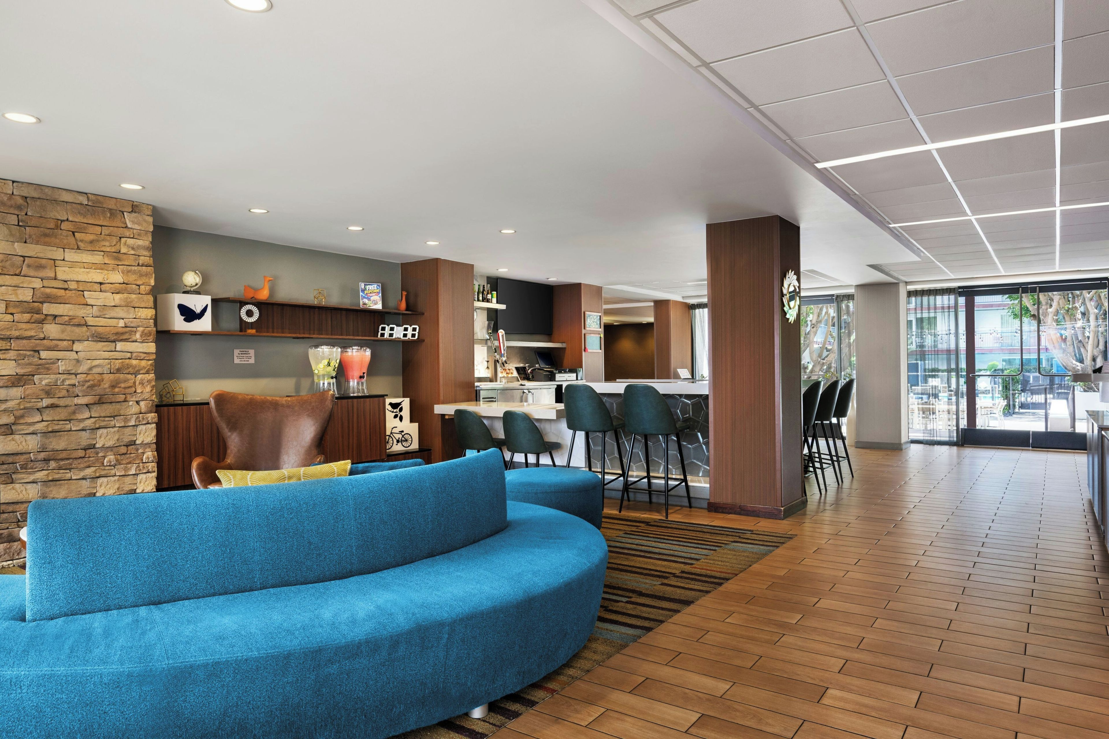 Een moderne hotellobby met een gebogen blauwe bank, een stenen accentmuur en een bar met krukjes.