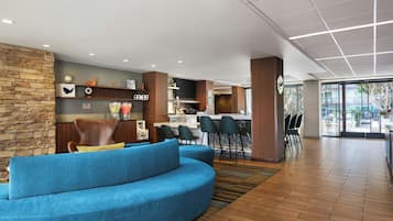 A modern hotel lobby with a curved blue sofa, a stone accent wall, and a bar area with stools.