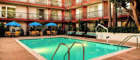 A hotel pool area with a clear pool, lounge chairs, and umbrellas.