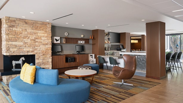 Un moderno vestíbulo de hotel con chimenea de piedra, un sofá azul, una mesa redonda y una zona de bar.